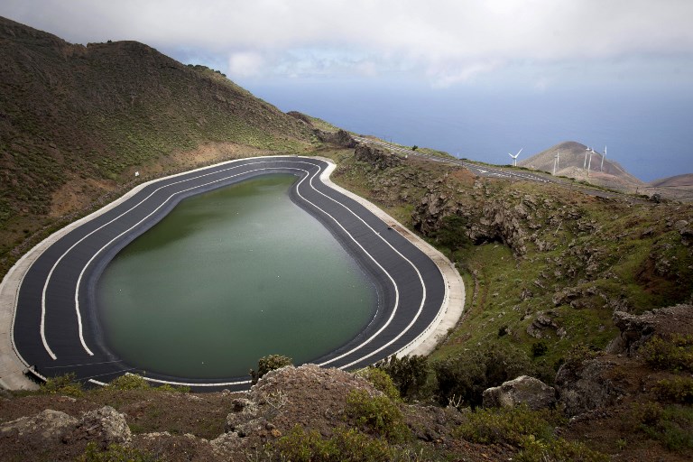 The pumped-storage power plant on the island of El Hierro, with an upper basin connected to the sea through a pump-turbine system. In the background are the wind turbines that power the pumps. 