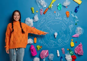 Femme souriante pointant une ampoule posée sur une terre dessinée et entourée de déchets