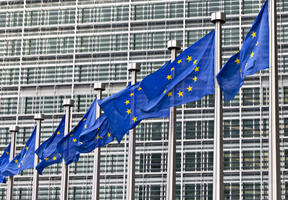 Image of the European Union headquarters in Brussels, behind a row of European flags.