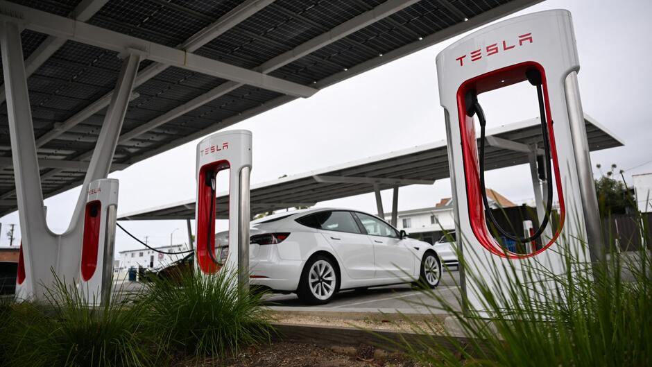 Tesla electric vehicles charging at charging stations located under solar panels at a Tesla Supercharger station in Santa Monica.
